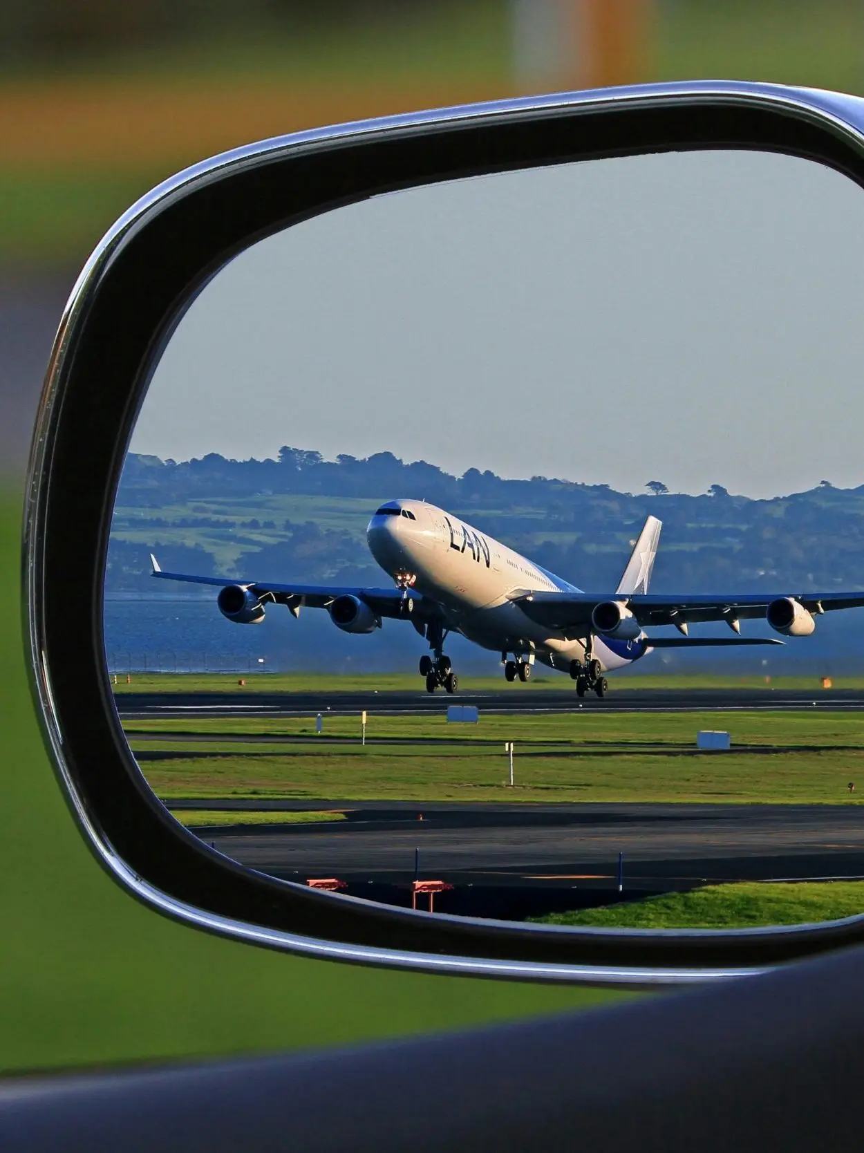 A jet airplane taking off is reflected in a car's side mirror, capturing a unique aviation perspective.